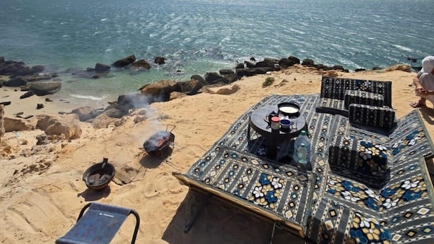 A beach with a patterned mat, a grill, and a metal chair. - oued ad dahab  (Dakhla)