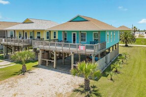 A two-story building with a balcony, a covered deck, and a sandy area in front.