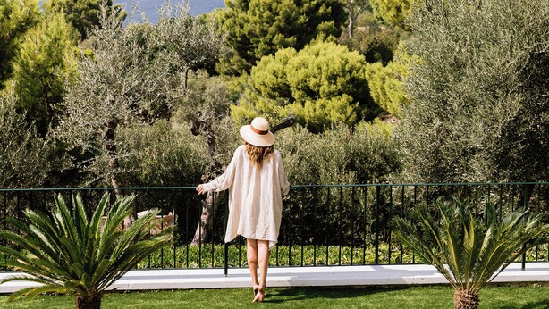 A person walking on a lawn with a view of the sea, surrounded by greenery and outdoor seating.
