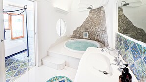 A bathroom with a bathtub, a sink, and a mirror. There is a stone wall and a door leading to another room.