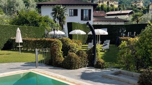 A swimming pool with clear water, surrounded by a well-maintained garden and a view of a hillside. - Bellagio Lake Home (Bellagio)
