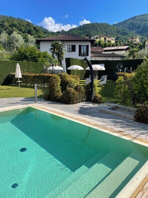 Una piscina con agua cristalina, rodeada de un jardín bien cuidado y vistas a una colina.