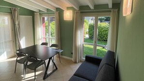 A room with a dining table, chairs, a sofa, a ceiling with wooden beams, and large windows with curtains. - Bellagio Lake Home (Bellagio)