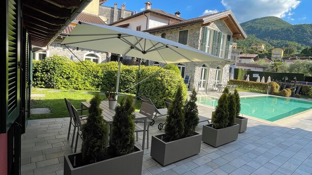 A patio with outdoor furniture, a swimming pool, and a view of buildings and mountains. - Bellagio Lake Home (Bellagio)