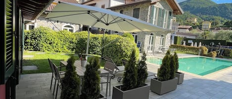 A patio with outdoor furniture, a swimming pool, and a view of buildings and mountains.