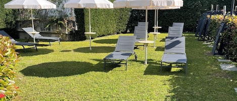 Un área exterior bien cuidada con sillones de relax y sombrillas, rodeada de exuberante vegetación y un paisaje montañoso.