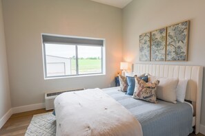 A bedroom with a large bed, a window with blinds, a radiator, and a wall-mounted lamp. - Airplane/Hanger Apartment 2 bedrooms 2 bathrooms #3 (Salado)