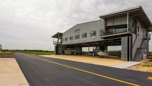 En stor industribygning med flere hangars, en belagt vej foran og en græsplæne i baggrunden.