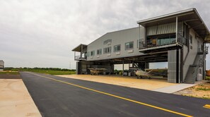A large industrial building with multiple hangars, a paved road in front, and a grassy field in the background. - Airplane/Hanger Apartment 2 bedrooms 2 bathrooms #3 (Salado)