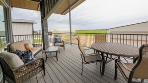 En overdækket terrasse med siddepladser og et bord, med udsigt over en grøn mark.
