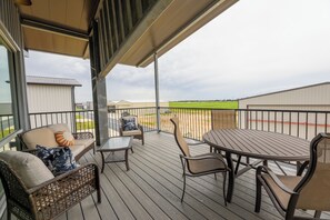 A covered outdoor deck with seating and a table, overlooking a green field. - Airplane/Hanger Apartment 2 bedrooms 2 bathrooms #3 (Salado)