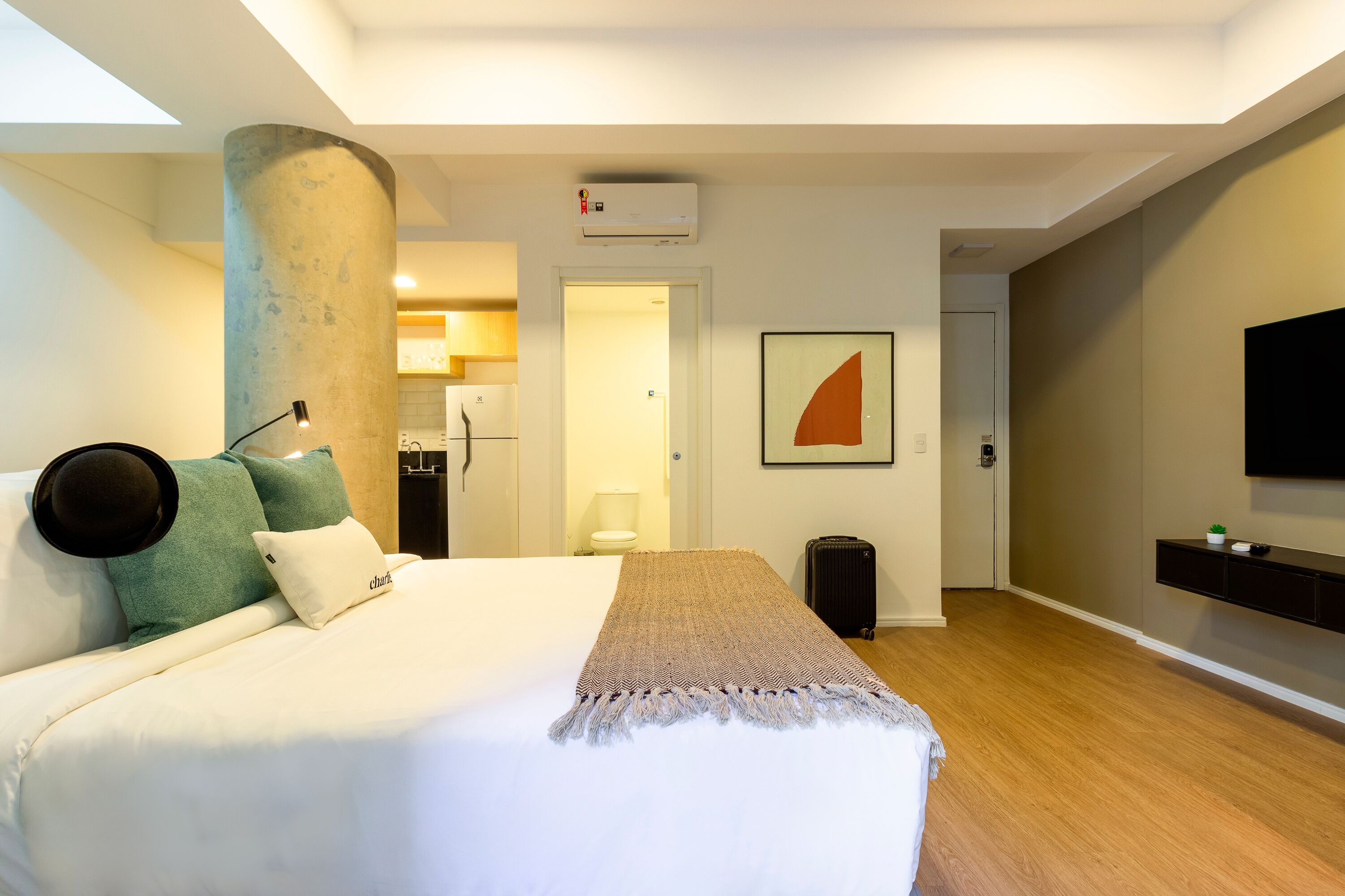 Ein Hotelzimmer mit Bett, einer Säule, einem an der Wand befestigten Fernseher und einer sichtbaren Tür zu einem Badezimmer.
