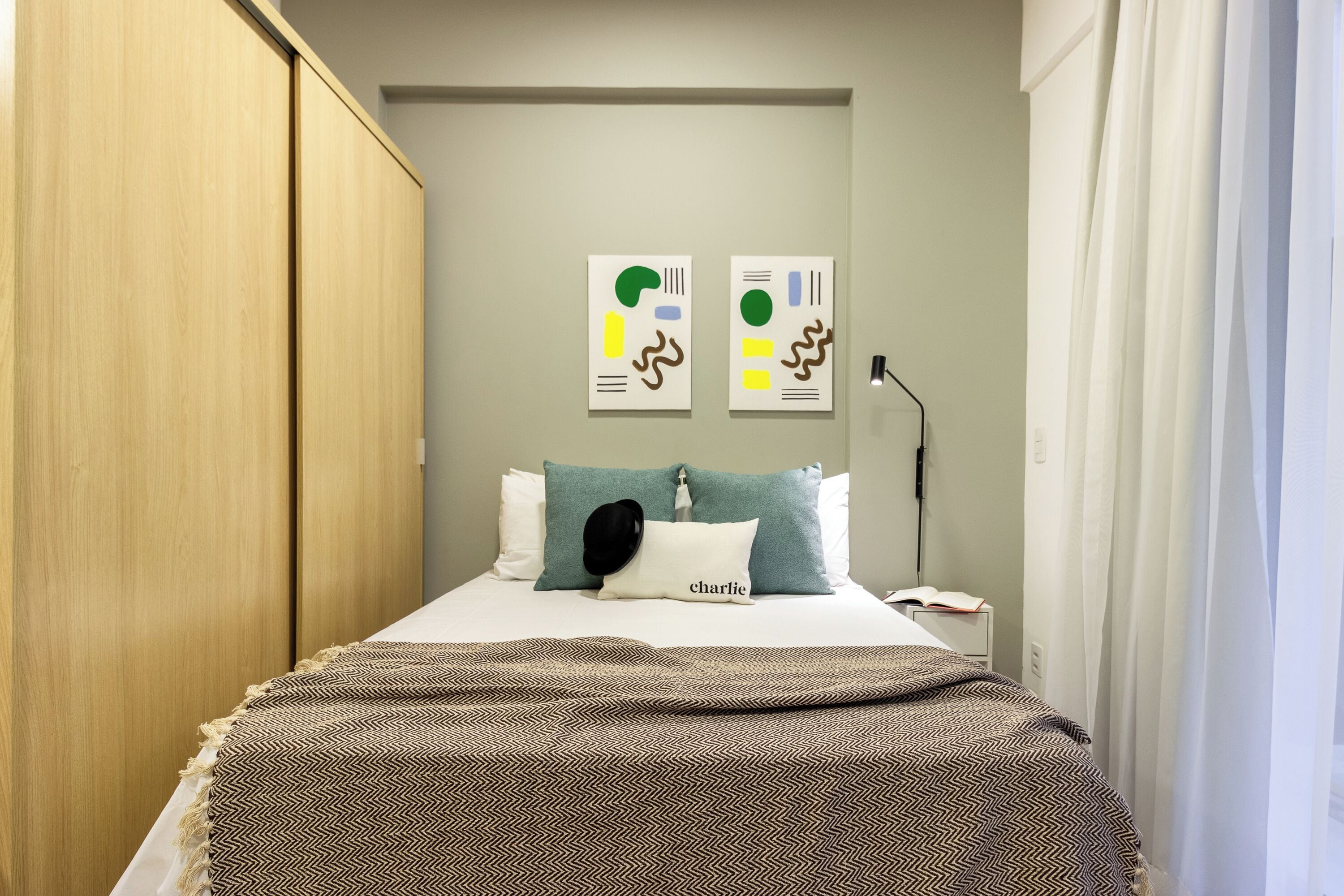 A bedroom with a bed, pillows, a bedside table, a lamp, and artwork on the wall.