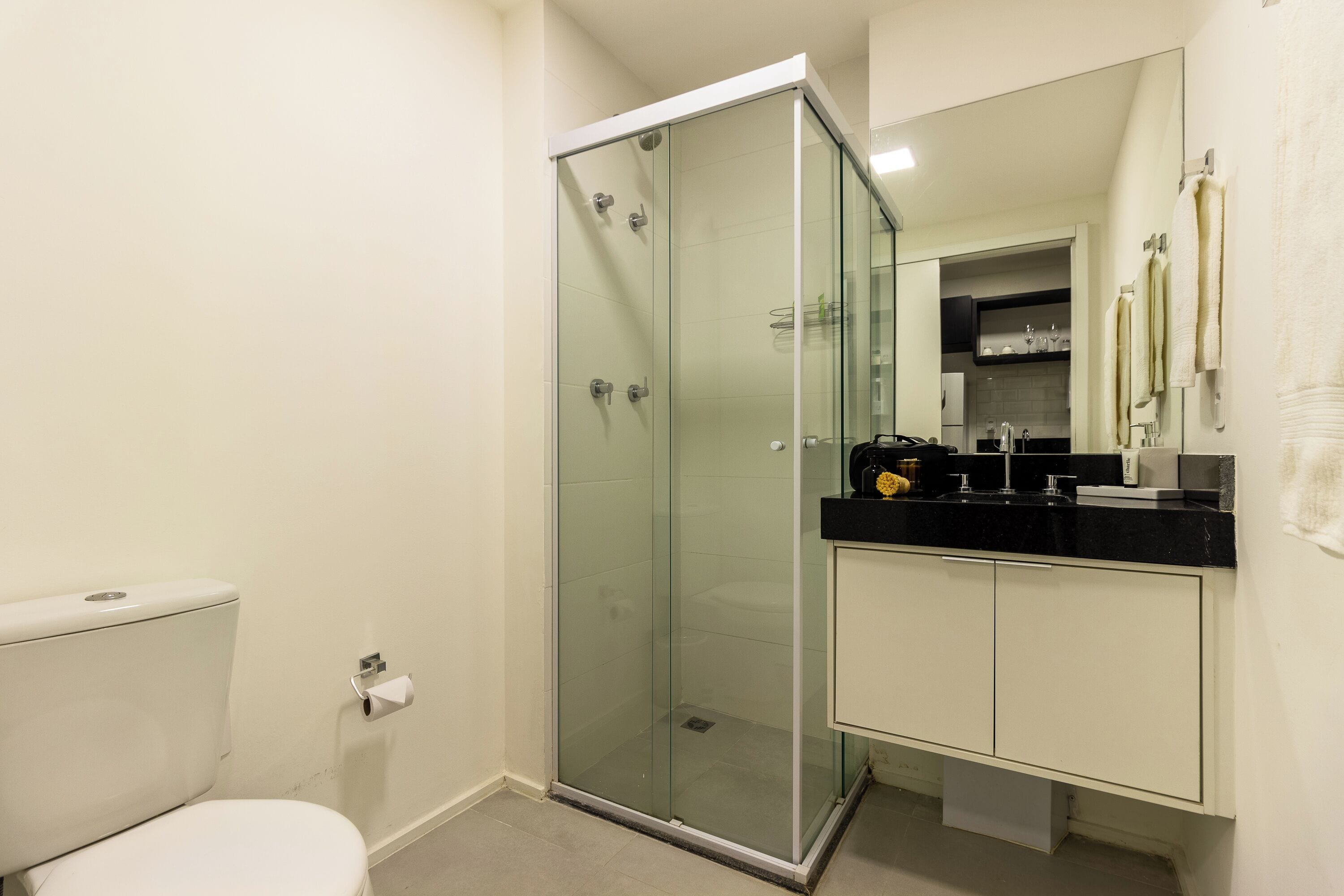 Une salle de bain moderne avec une douche à parois de verre, des toilettes blanches et un lavabo noir posé sur un plan de travail.