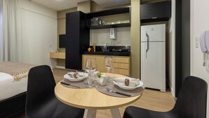 Ein Hotelzimmer mit einem Bett, einem Esstisch für zwei Personen, einer Küchenzeile inklusive Mikrowelle und Kühlschrank, sowie einer kleinen Pflanze auf der Arbeitsfläche.