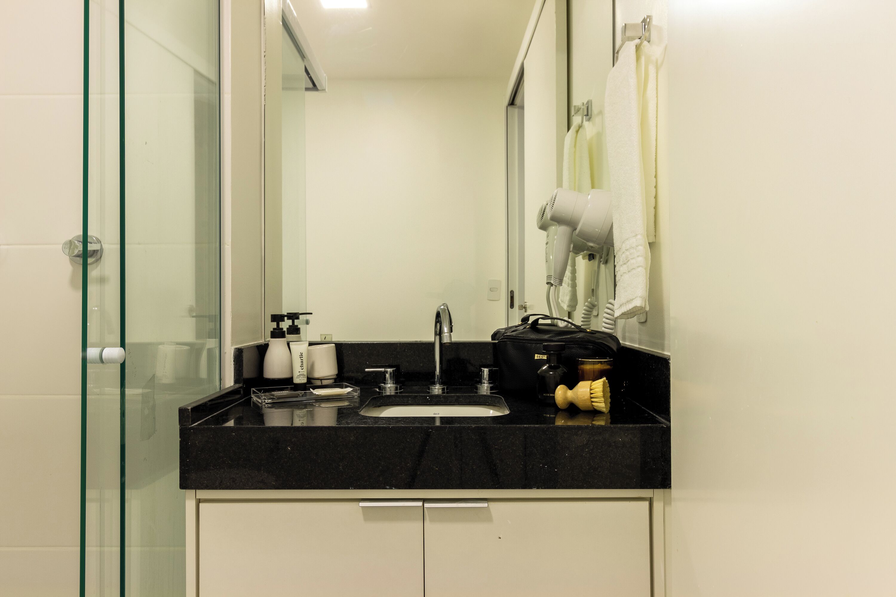 Une salle de bain avec une douche à parois de verre, un plan de toilette noir, un lavabo, un miroir et un sèche-cheveux.