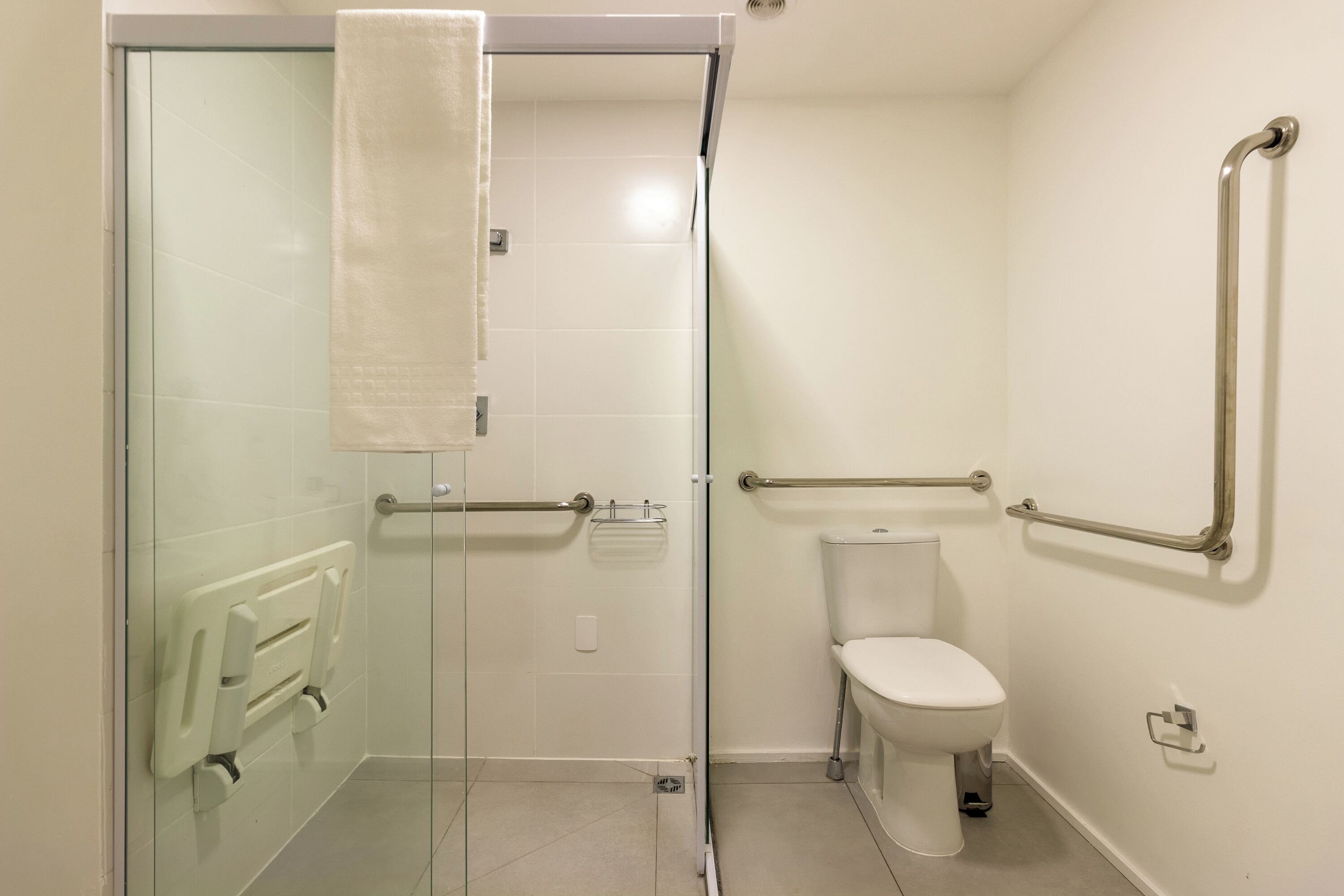 A bathroom with a glass shower enclosure, a white toilet, and handrails.