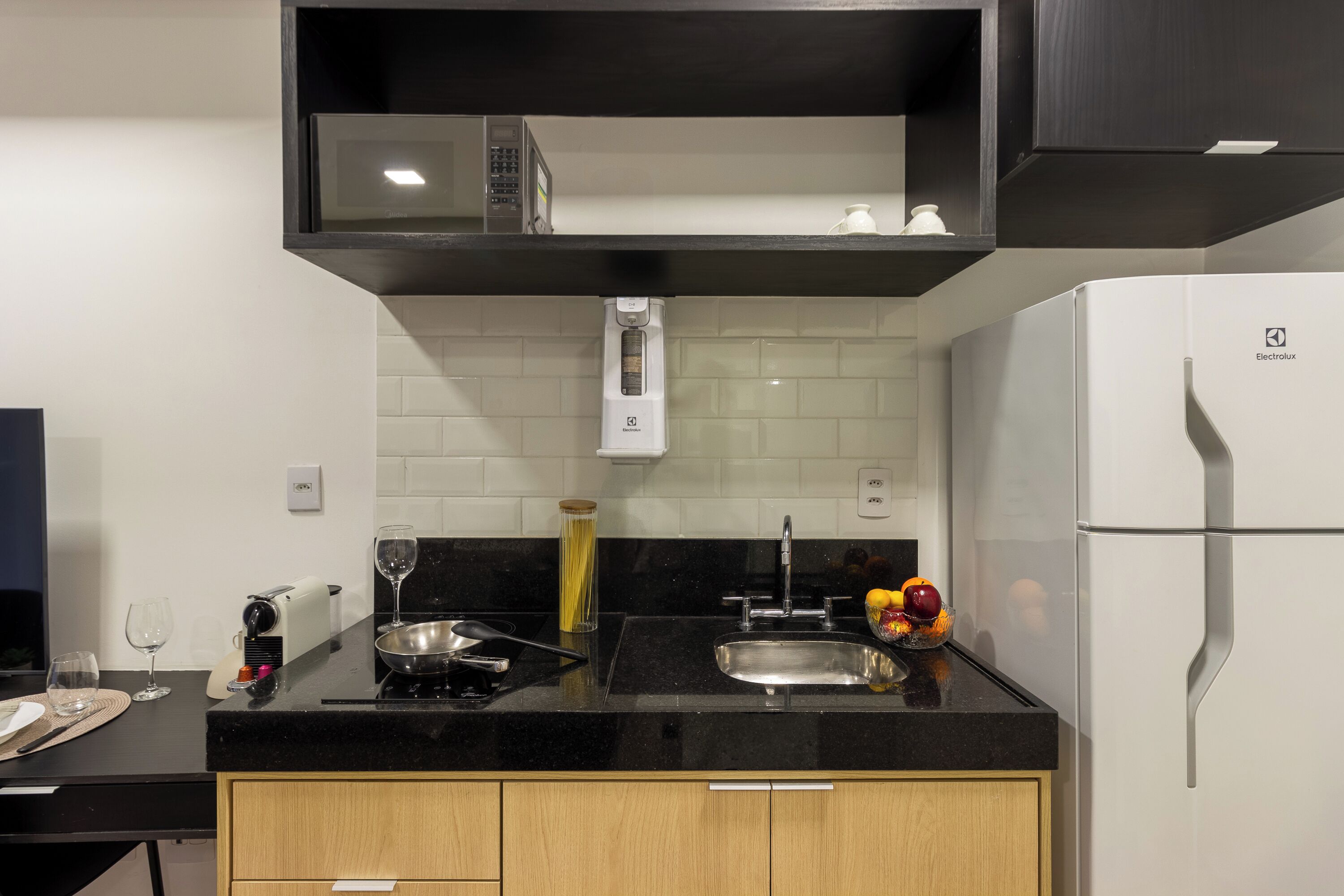 Una cocina moderna con encimera negra, pileta de acero inoxidable y refrigerador blanco.