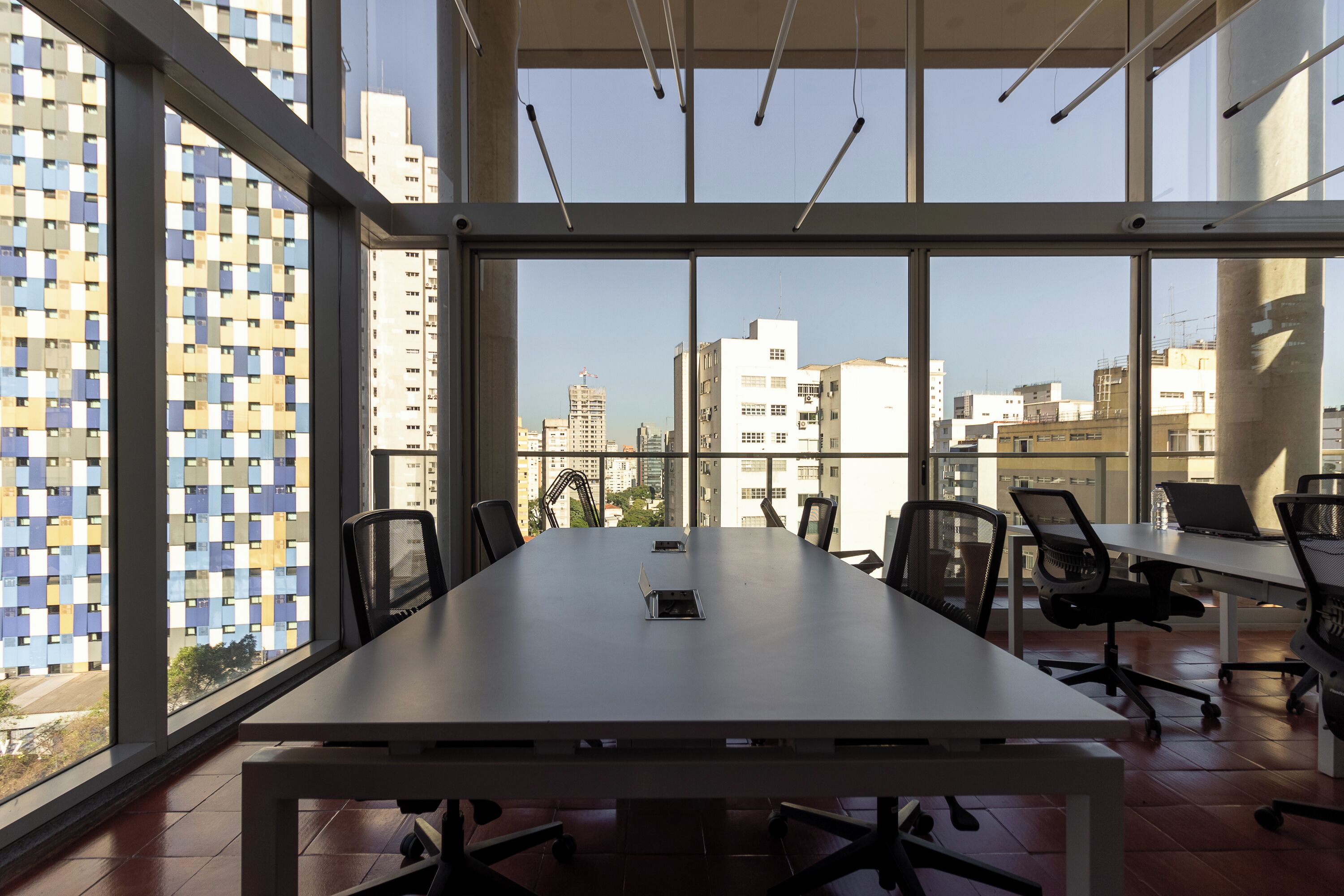 A conference room with a large table, chairs, and a view of a cityscape through large windows.