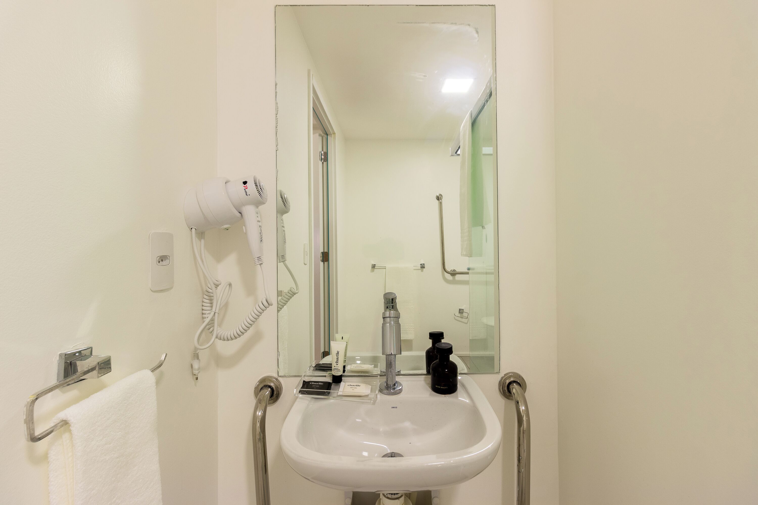 Un baño con lavamanos blanco, secador de pelo, espejo y toallero.