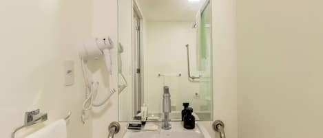 Un baño con lavamanos blanco, secador de pelo, espejo y toallero.