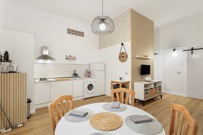 Eine moderne Küche mit weißen Schränken, einem eingebauten Ofen und einer Mikrowelle. Ein Essbereich mit einem runden Tisch und Stühlen ist ebenfalls vorhanden.