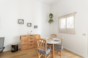 Ein Essbereich mit einem runden Tisch, Holzstühlen, einer kleinen Kommode und einer hängenden Pflanze.