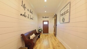Un corridoio con una panca di legno, una porta con l'indicazione 'Farmhouse' e un cartello che riporta la scritta 'La vita è breve, rendila dolce'.