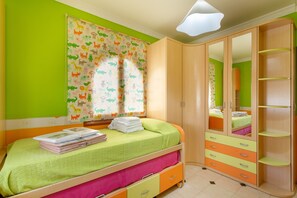 Quarto de criança com uma cama, um guarda-roupa e uma janela com cortina.