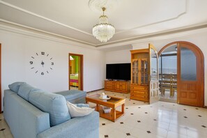 Ein Wohnzimmer mit einer Couch, einem Fernseher, einem Holzkabinett und einer Chandeliebre.