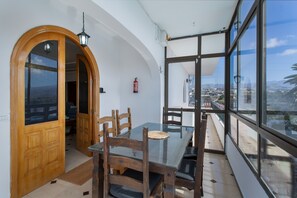 Ein Essbereich mit einem Glastisch, Holzsesseln und Blick auf eine Stadtlandschaft durch große Fenster.