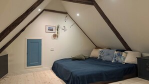 Une chambre avec un plafond en pente, un lit avec une literie bleue, une porte bleue et des éléments de décoration murale, notamment un tableau encadré et une sculpture d’oiseau.