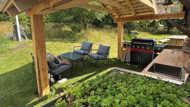 Une terrasse extérieure avec des poutres en bois, un barbecue et un espace détente comprenant des chaises et une table.