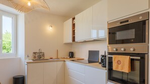 A modern kitchen with white cabinets, a built-in oven, a coffee machine, and a window providing natural light. - Charming house in Vallon Pont d'Arc with private terrace, garden, and Wi-Fi (Vallon-Pont-d'Arc)