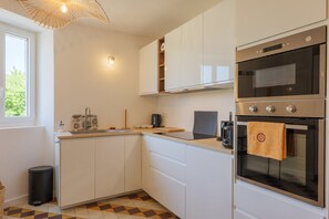 Una cocina moderna con armarios blancos, horno empotrado, cafetera y ventana que aporta luz natural.