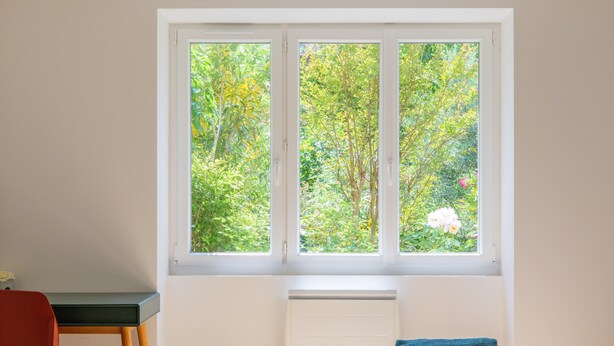 A room with a bed, a desk, and a window with a view of trees and flowers. - Charming house in Vallon Pont d'Arc with private terrace, garden, and Wi-Fi (Vallon-Pont-d'Arc)