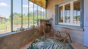 A balcony with wicker chairs, a large window with a view of greenery, and a rustic ceiling. - Charming house in Vallon Pont d'Arc with private terrace, garden, and Wi-Fi (Vallon-Pont-d'Arc)