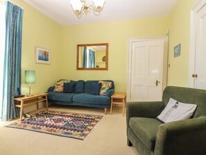 Ein Zimmer mit einer Couch, einem grünen Sessel, einem Teppich mit Muster, einer Lampe, einem Spiegel und einer Tür.
