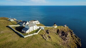 A coastal property with a lighthouse, white buildings, and a stone wall. - Lightkeepers Retreat (Eyemouth)