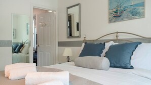 Een net opgemaakt bed met kussens en handdoeken, een bedlamp, een spiegel en een schilderij aan de muur.