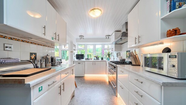 Een moderne keuken met witte kastjes, een centraal eiland en uitzicht op groen.