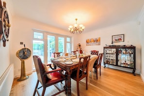A dining room with a wooden table set for six, surrounded by chairs, a chandelier, and a cabinet with glass doors.