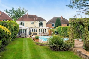 A residential property with a swimming pool, a covered patio, and a well-maintained lawn.