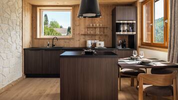A modern kitchen with a central island, wooden cabinetry, a built-in oven, and a window overlooking greenery.