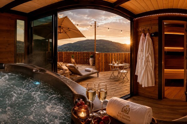 Een hottub met uitzicht op bergen, een houten terras met ligstoelen en een tafel met glazen en aardbeien.