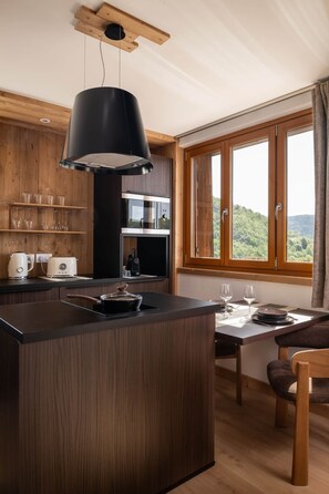 A modern kitchen with wooden cabinets, a central island, and a large window with a view of the outdoors. - Bellevue - Private Sauna & Jacuzzi (La Bresse)