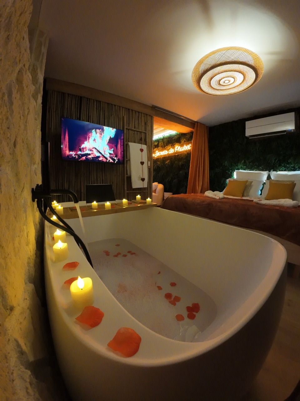 A modern bathroom with a freestanding bathtub, candles, and a television.