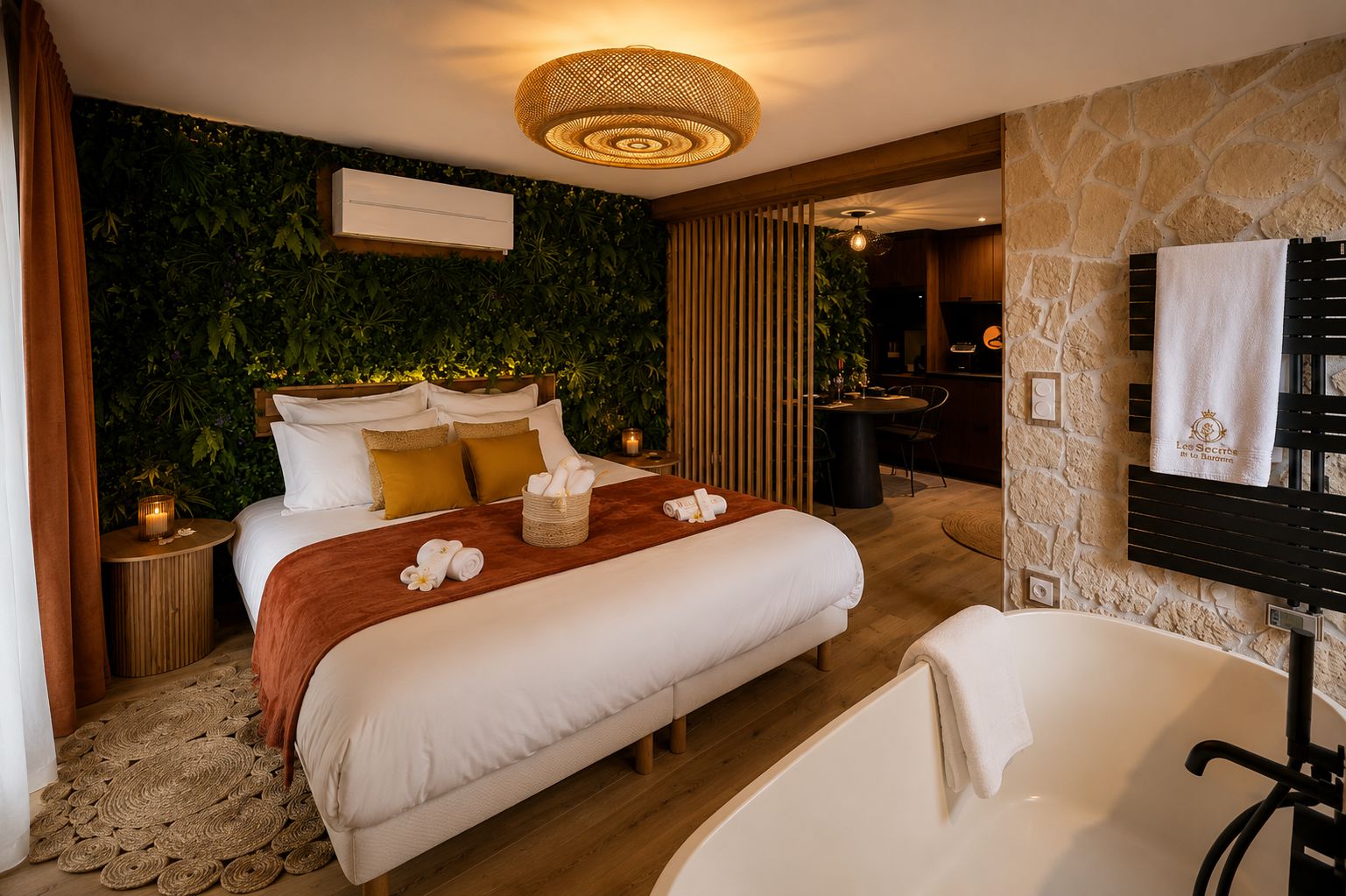 Une chambre d’hôtel moderne dotée d’un grand lit, d’une salle de bain avec baignoire, d’un coin repas et d’un mur végétal.