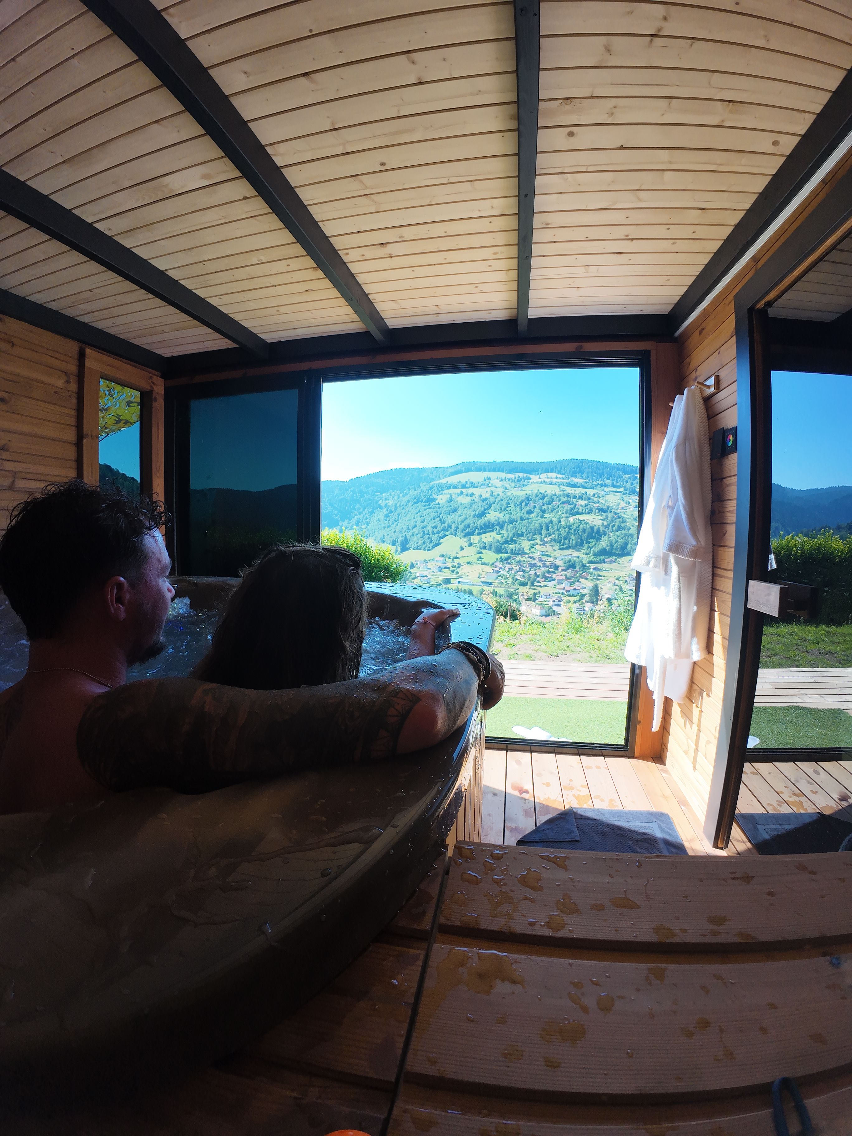 A person relaxing in a hot tub with a view of a mountainous landscape through a large window.