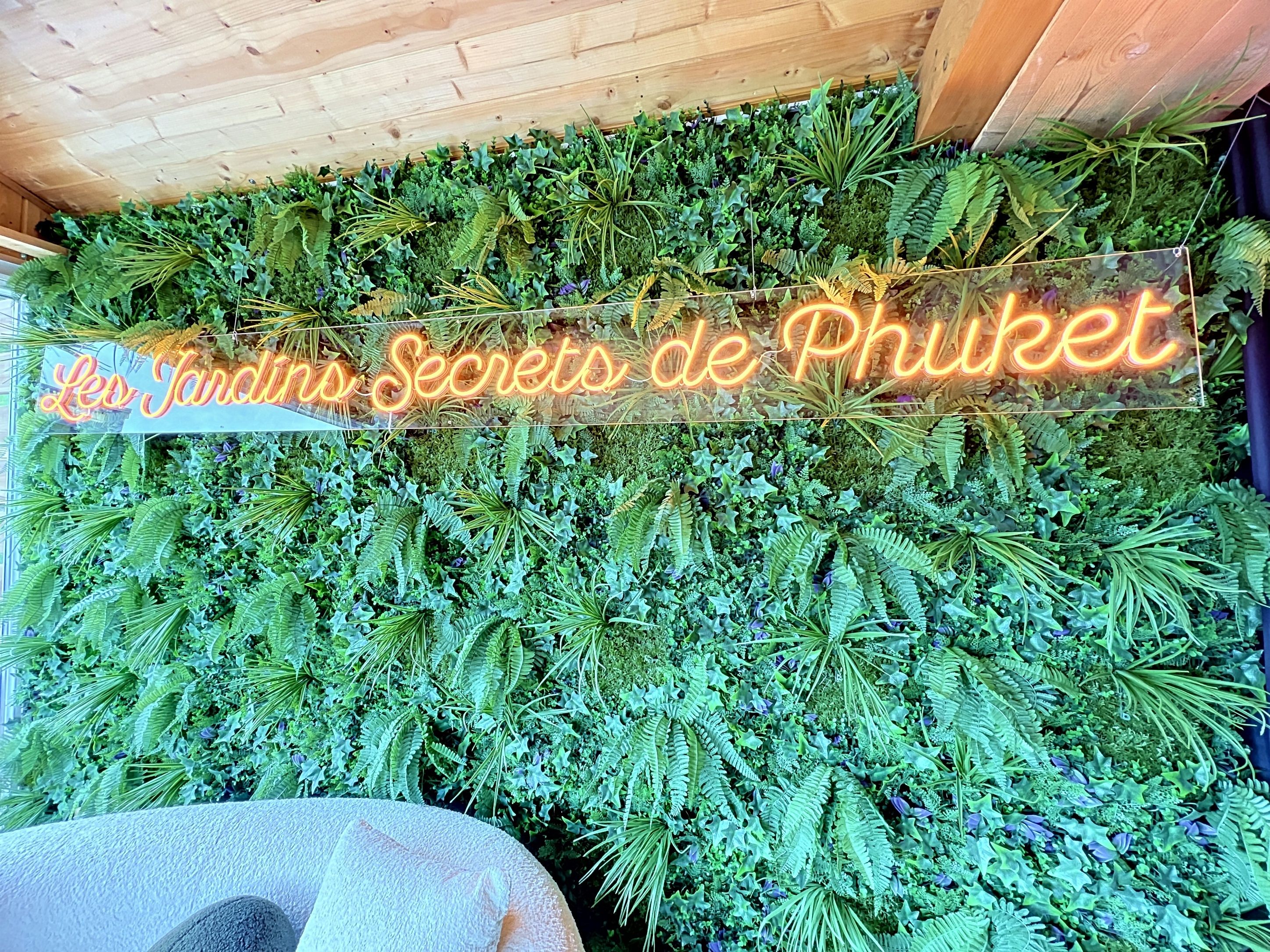Una pared con un letrero de neón que dice 'Lee Jindian's Secrets de Phuket' y una densa composición de follaje verde.